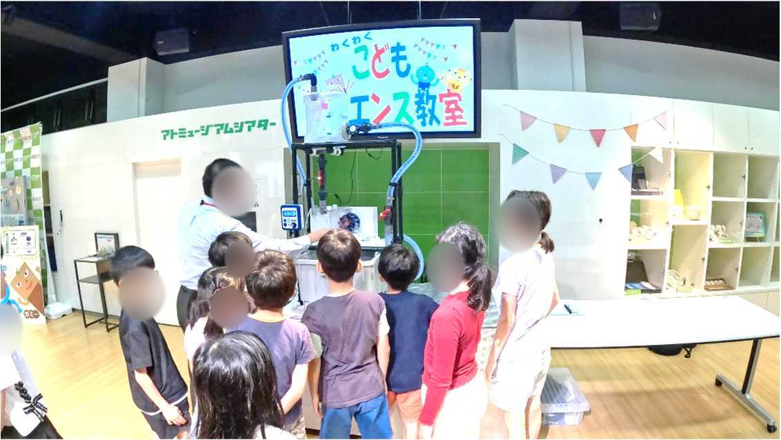 水力発電キットを囲んで佐藤教授の実演を見学する子どもたち。人物の顔は自然な輪郭でぼかしています。